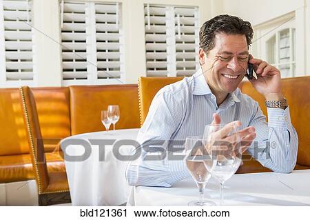 Stock Image - Caucasian businessman on cell phone at restaurant. Fotosearch