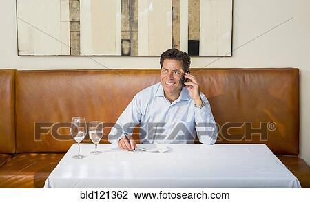 Stock Image - Caucasian businessman on cell phone at restaurant. Fotosearch