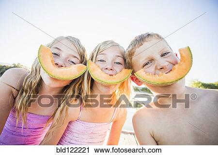 Stock Image - Caucasian children eating cantaloupe slices. Fotosearch