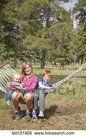 Stock Photograph - Caucasian children sitting in hammock outdoors. Fotosearch