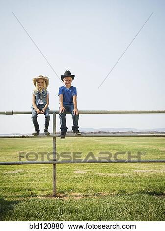 Stock Image - Caucasian children sitting on fence on farm. Fotosearch