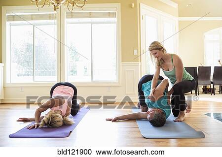Stock Image - Caucasian couple working with yoga instructor in home. Fotosearch
