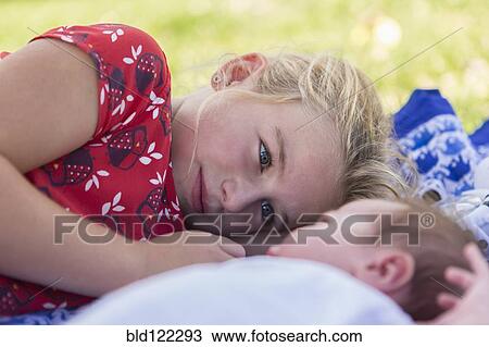 Stock Image - Caucasian girl laying with newborn baby brother. Fotosearch