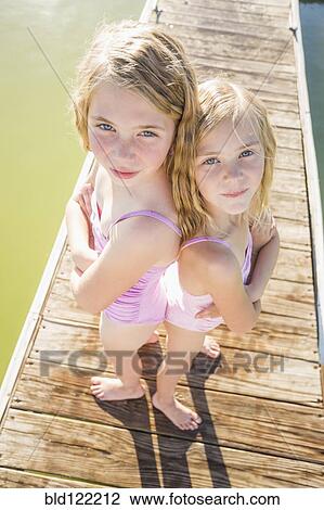 Stock Image - Caucasian girls standing back to back on dock. Fotosearch
