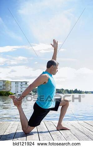 Picture - Caucasian man practicing yoga on wooden dock. Fotosearch