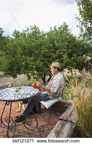 Stock Image - Caucasian man reading at table outdoors. Fotosearch