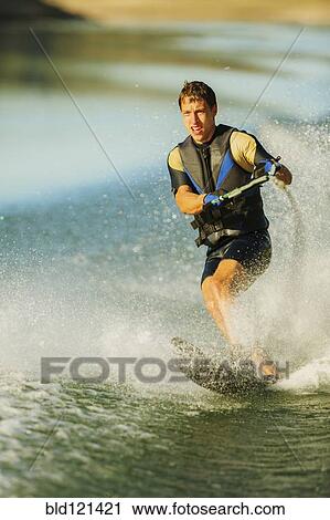 Stock Image - Caucasian man water skiing on lake. Fotosearch