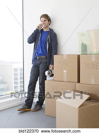 Stock Image - Caucasian man with cardboard boxes in new home. Fotosearch