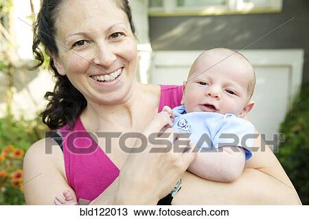 Stock Image - Caucasian mother holding newborn son outdoors. Fotosearch