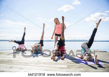 Stock Photo - Caucasian people practicing yoga on wooden dock. Fotosearch
