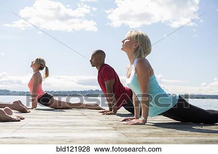 Caucasian people practicing yoga on wooden dock View Large Photo Image Stock Photo - Caucasian people practicing yoga on wooden dock. Fotosearch