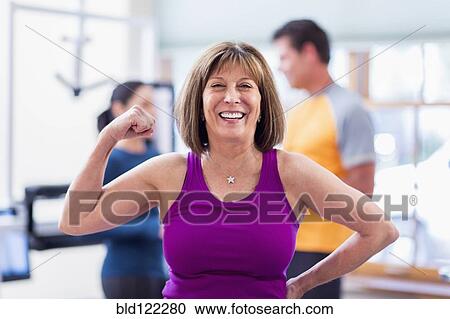 Stock Image - Caucasian woman flexing her muscles in gym. Fotosearch