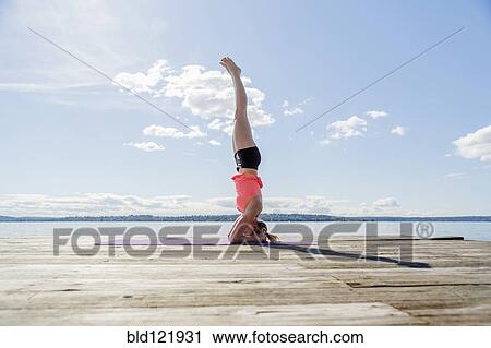 Stock Image - Caucasian woman practicing yoga on wooden dock. Fotosearch