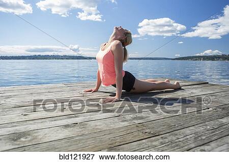 Stock Photo - Caucasian woman practicing yoga on wooden dock. Fotosearch