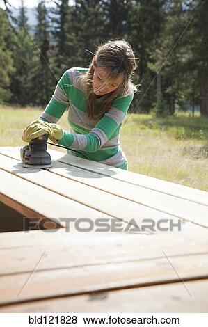 Stock Photo - Caucasian woman sanding wood outdoors. Fotosearch