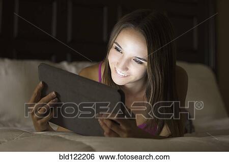 Stock Photograph - Caucasian woman using digital tablet in bed. Fotosearch