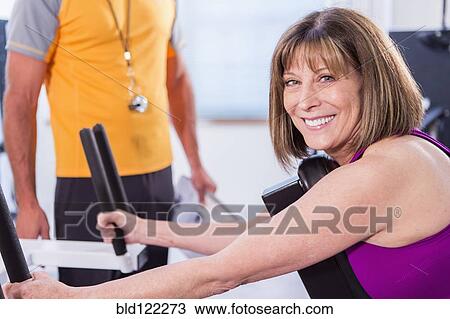 Stock Image - Caucasian woman working with personal trainer in gym. Fotosearch