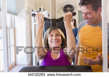 Stock Image - Caucasian woman working with personal trainer in gym. Fotosearch