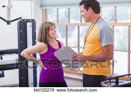 Stock Photo - Caucasian woman working with personal trainer in gym. Fotosearch