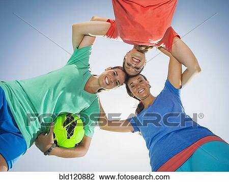 Stock Image - Caucasian women smiling in huddle under blue sky. Fotosearch