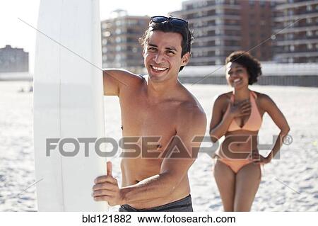 Stock Image - Couple with surfboard on beach. Fotosearch