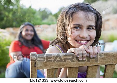 Stock Image - Girl smiling in wooden chair outdoors. Fotosearch