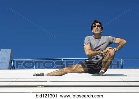 Stock Image - Hispanic athlete stretching on bleachers. Fotosearch