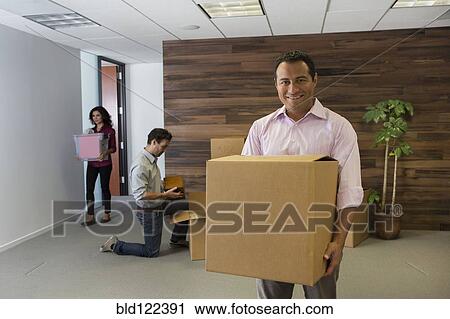 Stock Image - Hispanic businessman carrying cardboard box in office. Fotosearch