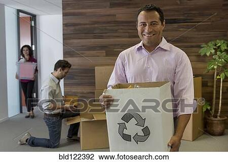 Stock Image - Hispanic businessman carrying cardboard box in office. Fotosearch