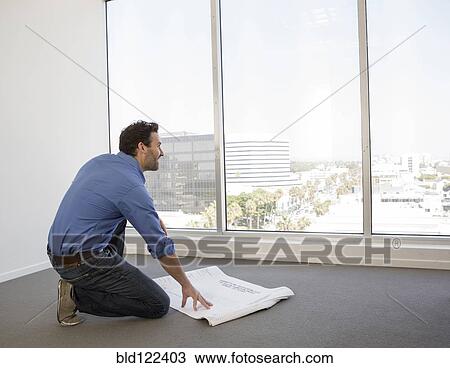 Stock Image - Hispanic businessman examining blueprints in office. Fotosearch