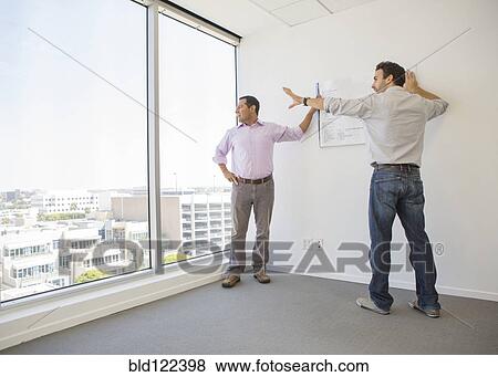 Stock Photo - Hispanic businessmen examining blueprints in office. Fotosearch