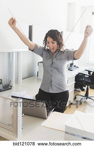 Stock Photo - Hispanic businesswoman cheering in office. Fotosearch
