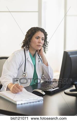 Stock Image - Hispanic doctor working in office. Fotosearch