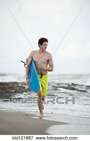 Hispanic man carrying surfboard on beach View Large Photo Image Stock Photo - Hispanic man carrying surfboard on beach. Fotosearch