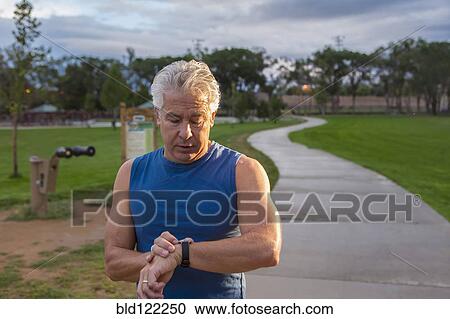 Stock Image - Hispanic man checking his watch in park. Fotosearch