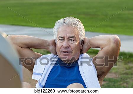 Stock Image - Hispanic man doing sit-ups in park. Fotosearch