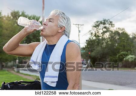 Stock Photo - Hispanic man drinking water in park. Fotosearch