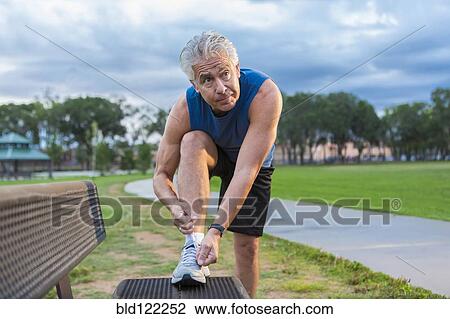 Stock Image - Hispanic man tying shoe in park. Fotosearch