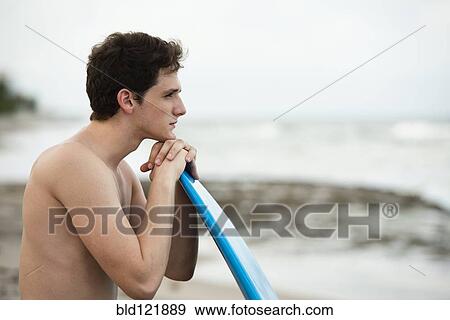 Stock Photo - Hispanic man with surfboard on beach. Fotosearch