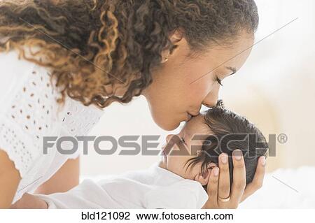Stock Image - Hispanic mother kissing baby's forehead. Fotosearch
