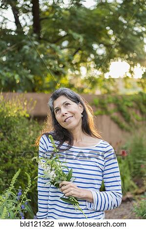 Stock Image - Hispanic woman holding flowers in garden. Fotosearch