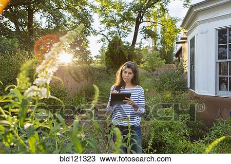 Stock Image - Hispanic woman sketching flowers in garden. Fotosearch