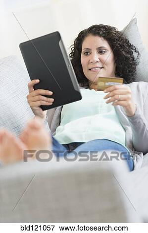 Stock Photo - Hispanic woman using digital tablet on sofa. Fotosearch