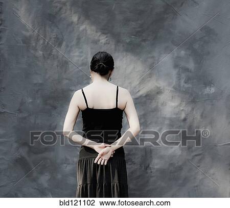 Stock Image - Japanese woman standing by gray curtain. Fotosearch