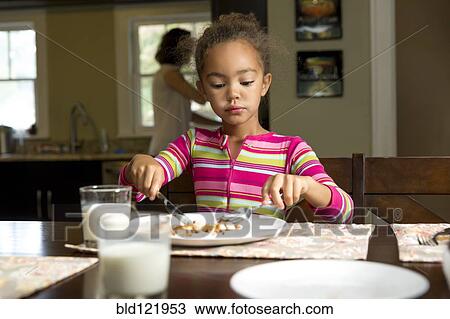 Stock Image - Mixed race girl eating at table. Fotosearch
