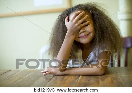 Stock Image - Mixed race girl laughing at table. Fotosearch