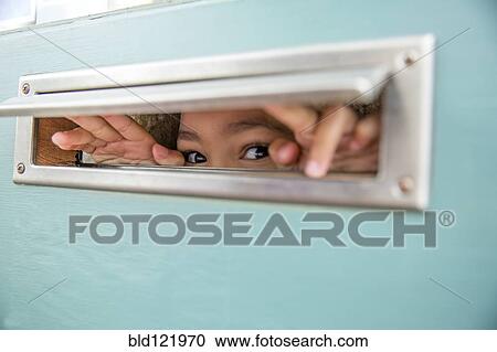 Stock Image - Mixed race girl peeking through mail slot. Fotosearch