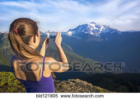 Stock Photography - Mixed race girl photographing mountains, North Cascade Mountains, Washington, United States. Fotosearch