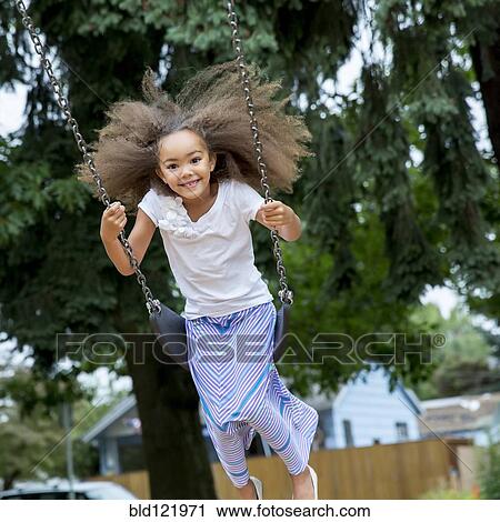 Stock Image - Mixed race girl playing on swing. Fotosearch