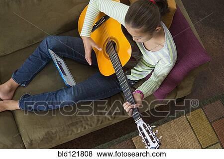 Stock Photo - Mixed race girl practicing guitar on sofa. Fotosearch